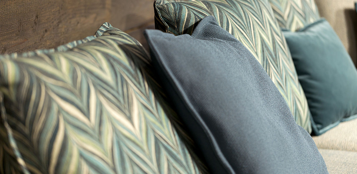 Nahaufnahme von dekorativen Kissen in Blau und Grün, mit verschiedenen Mustern und Texturen, auf einem Sofa arrangiert