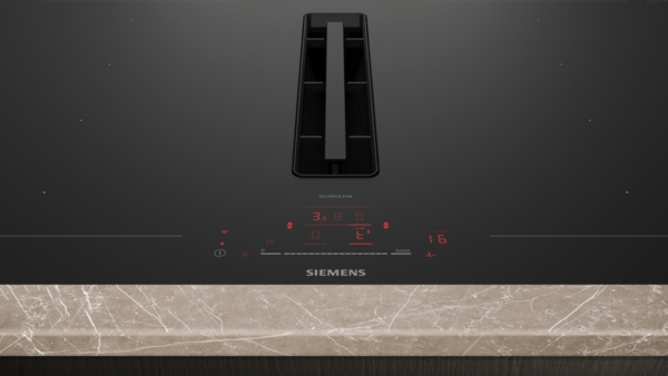 Nahaufnahme der Bedienfläche und des zentralen Dunstabzugs des schwarzen Siemens StudioLine Induktionskochfelds. Die rote Digitalanzeige zeigt die Einstellungen "3. E." und "6" an.