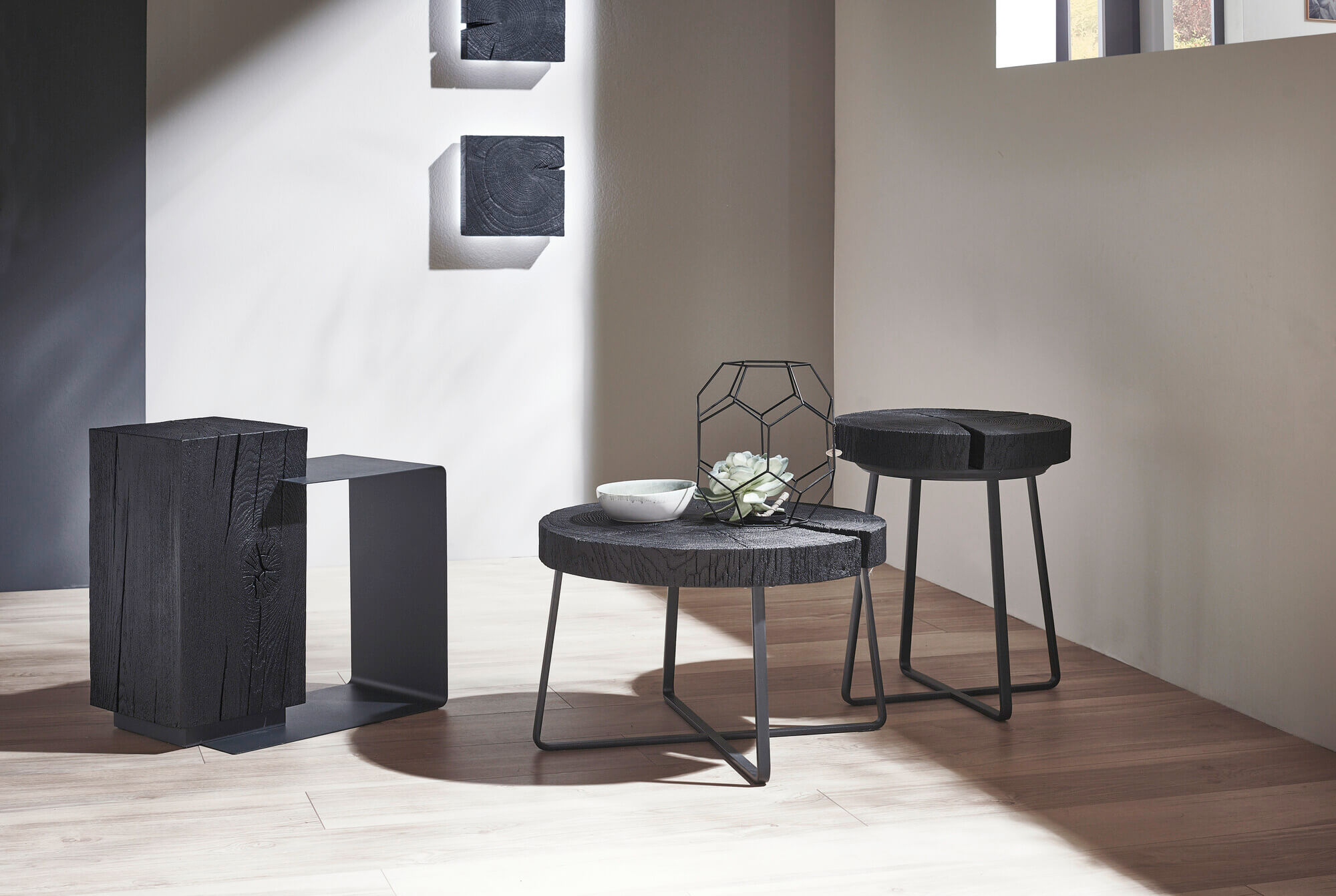 Stilvolles Wohnzimmer mit schwarzen Couchtischen aus Holz, dekoriert mit geometrischem Metallobjekt und kleiner Pflanze.