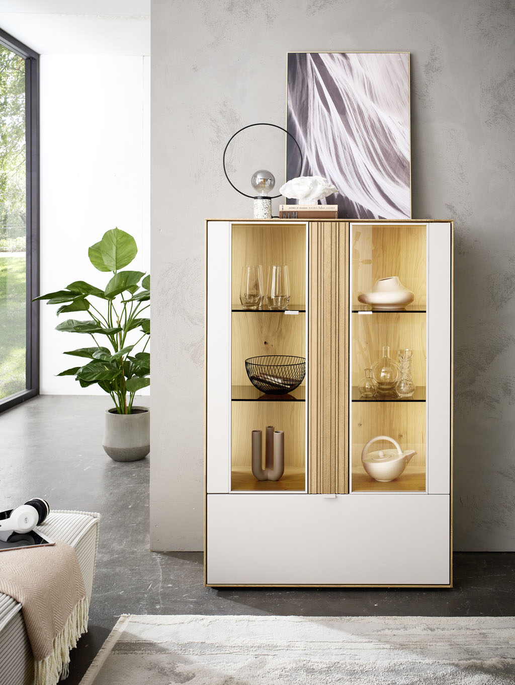 modernes Highboard mit Vitrinenausschnitt und Beleuchtung in braun-weiß stilvoll dekoriert in einem hellen Raum