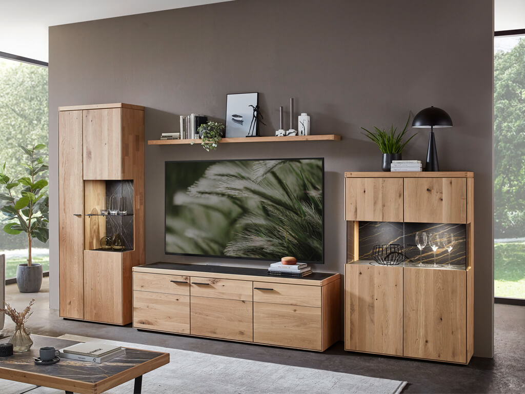 Mehrteilige Wohnwand aus hellem Eichenholz an einer grauen Wand, bestehend aus Standvitrine, Lowboard, Wandboard und Highboard.
