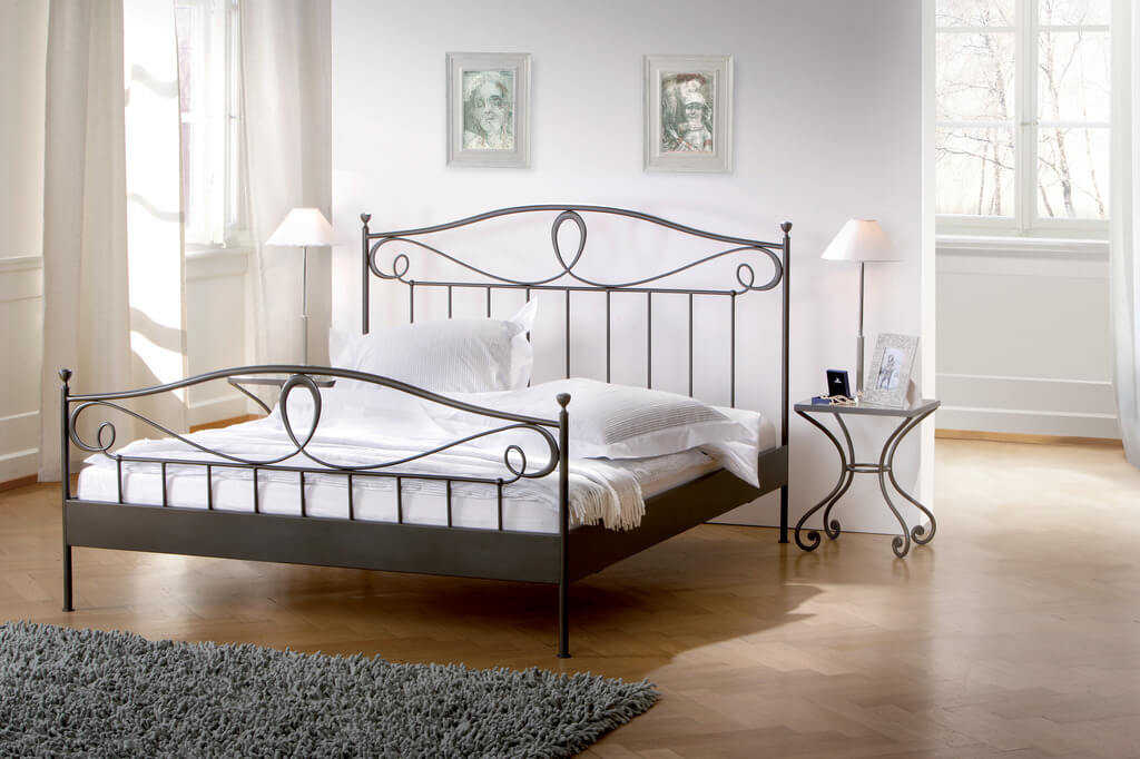 schwarzes Eisenbett mit weißer Bettwäsche und einem passenden Nachttisch stilvoll dekoriert in einem hellen Zimmer