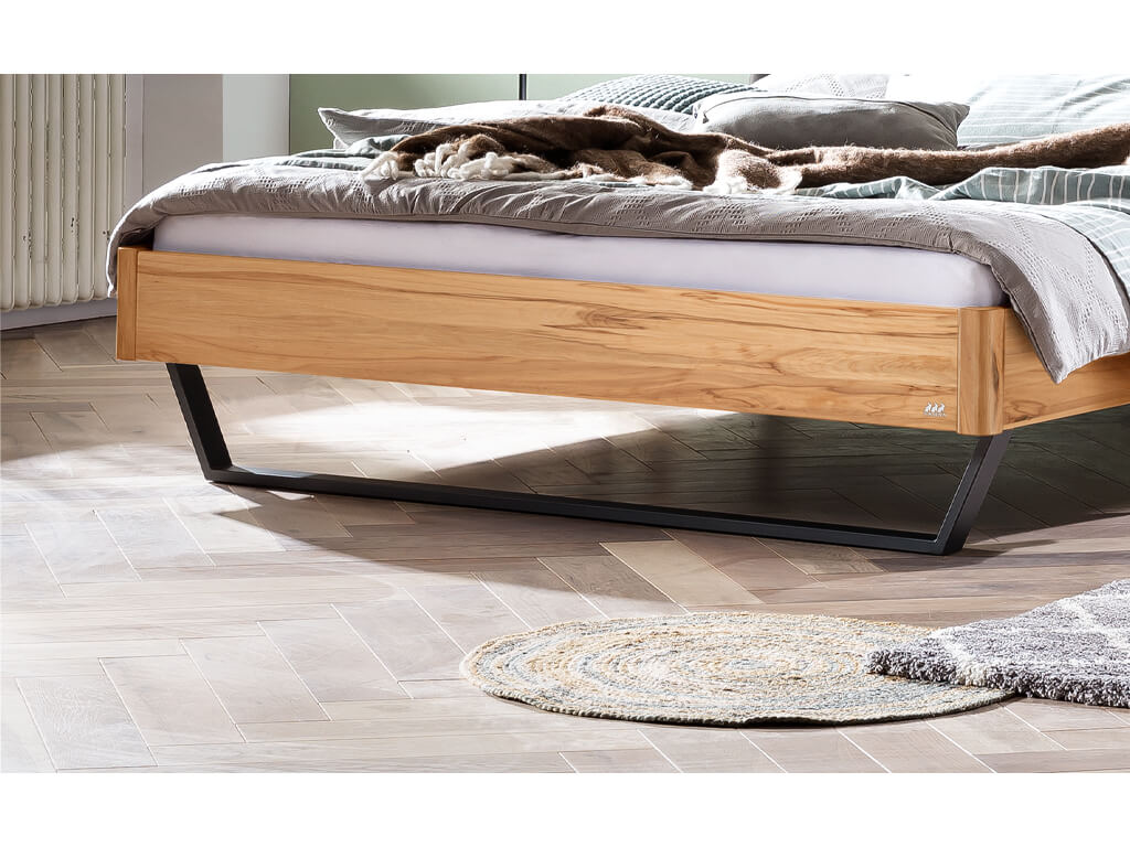 Nahaufnahme des Fußendes eines Bettes mit einem Gestell aus Wildbuche. Die Maserung des Holzes ist deutlich zu erkennen. Das Bett steht auf einem schwarzen Metallgestell.