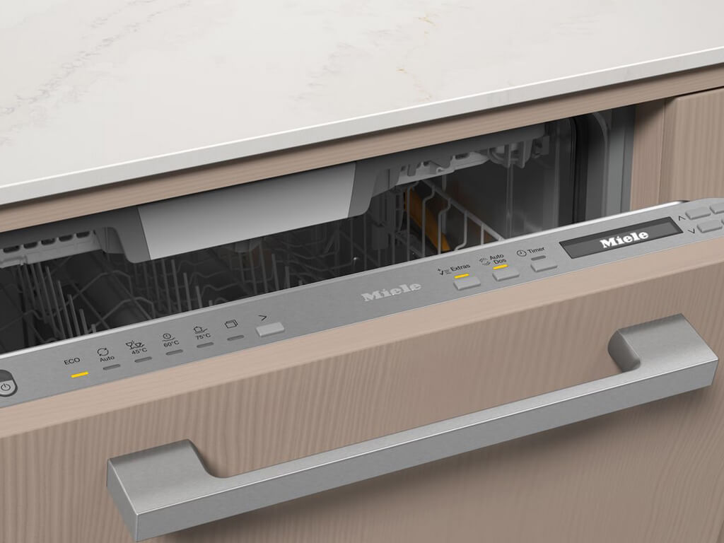 Nahaufnahme des oberen Bereichs eines geöffneten Miele Geschirrspülers, der in eine Küchenzeile mit heller Holzfront integriert ist.