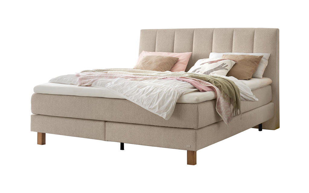 Ein Boxspringbett in hellem Beige mit einem gesteppten Kopfteil, freigestellt auf weißem Hintergrund.