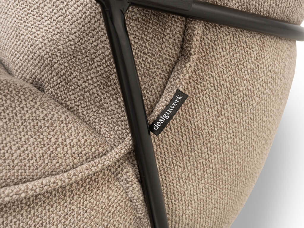 Nahaufnahme eines beigefarbenen Stoffsessels mit schwarzem Metallrahmen und Designwerk Etikett