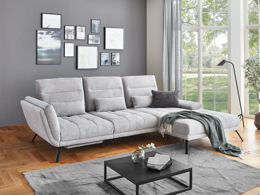 Poco Dayton - Polstergarnitur | Eckkombination | B: 295 cm Modernes Wohnzimmer mit grauem Sofa, Dekokissen und Decke, umgeben von großen Fenstern und stilvoller Wanddekoration