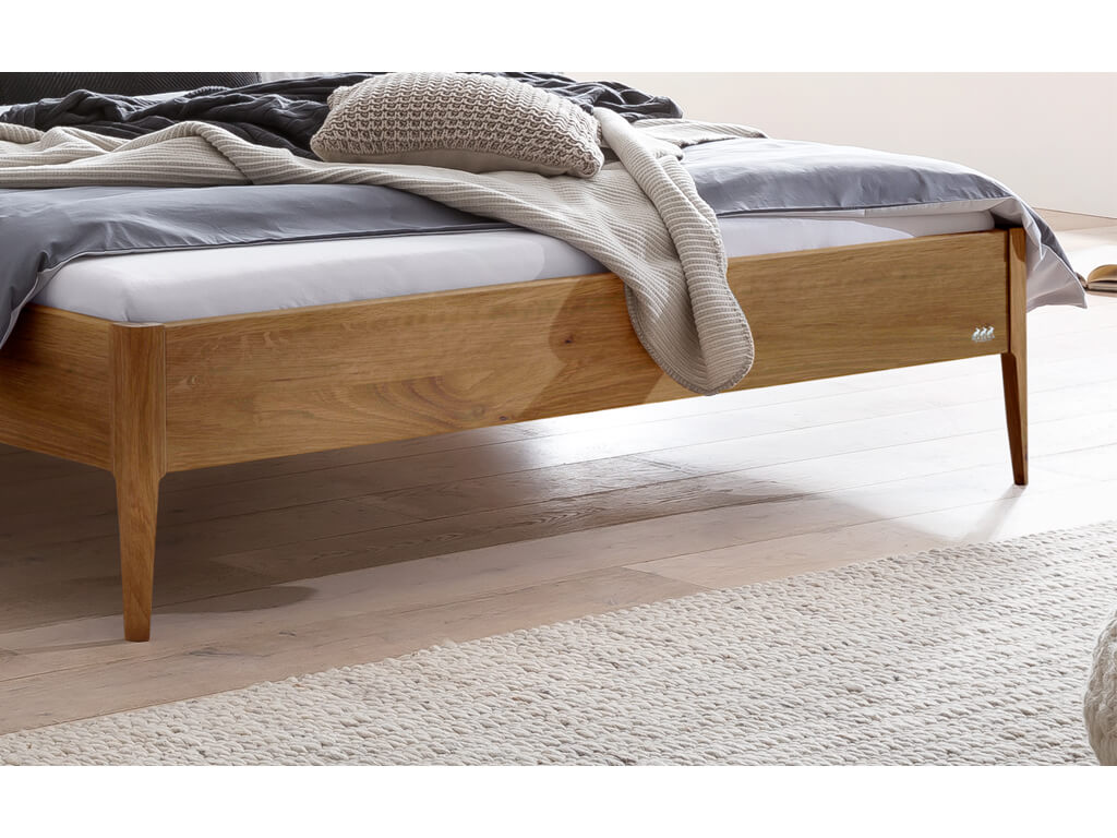 Eine Nahaufnahme der Fußpartie des Bettes "Busseto". Das Bett hat einen Rahmen aus natur geölter Wildeiche und steht auf konischen Holzfüßen.