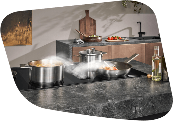 Kochfeld mit Topf und Pfanne bei denen der Dunst über einen Kochfeldabzug gezogen wird.