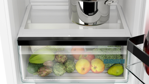 Offener Kühlschrank zeigt Gemüsefach mit Artischocken, Äpfeln, Brokkoli und einem Kochtopf auf dem Regal