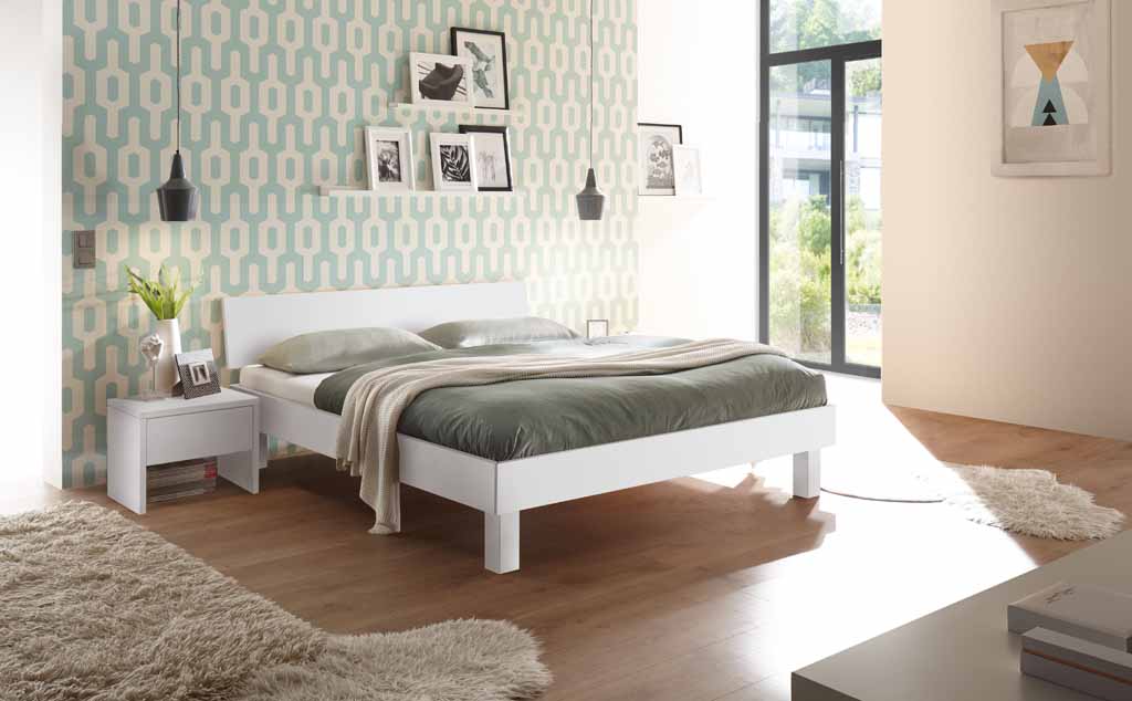 Hasena Trento - Bett Forti | Buche weiß, deckend lackiert Helles Schlafzimmer mit weißen Möbeln, grüner Bettwäsche, holzboden und modernem Tapetenmuster