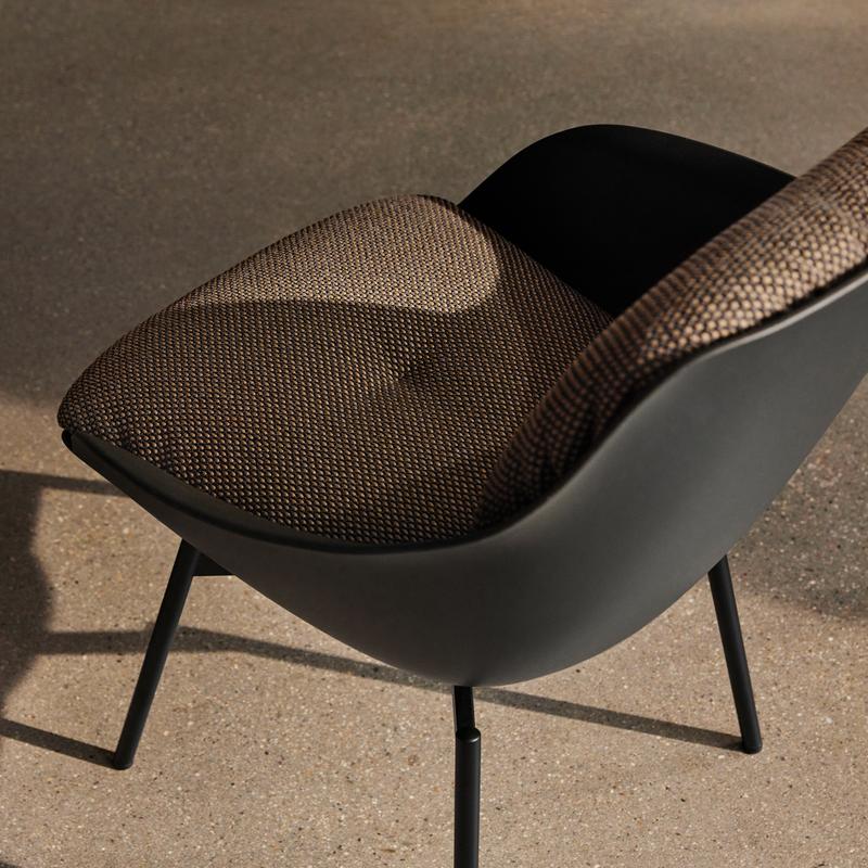 Ein moderner Designerstuhl mit gepolstertem, gemustertem Sitzbezug, schwarzem Rahmen und Metallbeinen auf Betonboden.