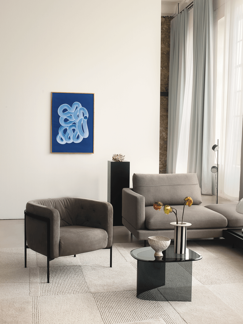 Wohnzimmer mit grauem Sessel, Sofa, Glastisch und blauem Gemälde an der weißen Wand