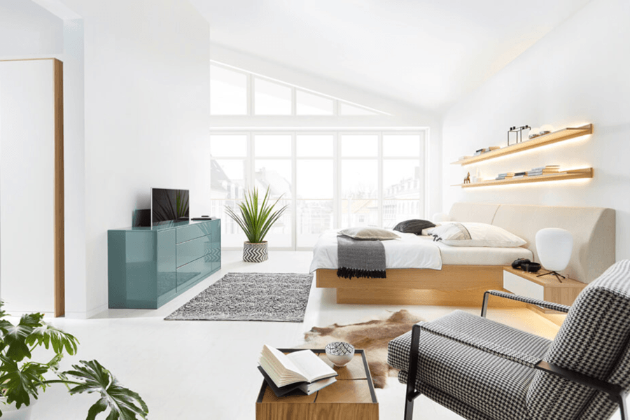 Schlafzimmer komplett in weiß mit grün/blauem Sideboard mit Fernseher, der gerade aus dem Sideboard heraus fährt.