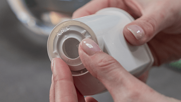 Nahaufnahme von Händen, die die verstellbare Aroma-Ring-Einstellung mit den Buchstaben A, B und C am Boden des Wasserfilters justieren, hervorgehoben durch einen türkisfarbenen Kreis.