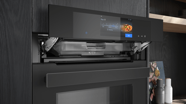 Detailansicht der angehobenen Bedienblende des Siemens Backofens. Dahinter wird der Wassertank für die Dampffunktion sichtbar.