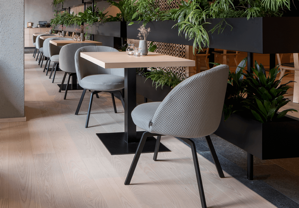 Cafe mit mehreren Holz Tischen und Polsterstühlen in hellgrau