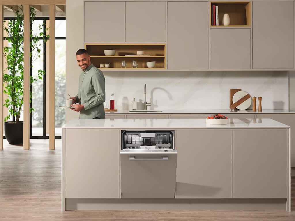 Ein Mann steht lächelnd in einer modernen Küche mit einer Geschirrspülmaschine in der Kücheninsel, die leicht geöffnet ist.