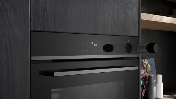 Detailaufnahme der Bedienblende eines schwarzen Einbaubackofens (Siemens studioLine). Das Display zeigt 160C an. Der rechte Bedienknebel ist transparent und ragt leicht heraus. Die Front ist in dunkle Küchenmöbel integriert.