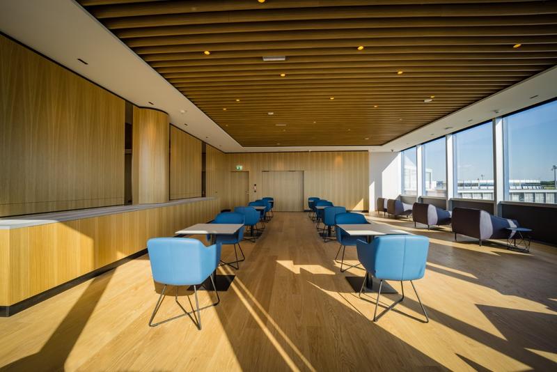 Ein geräumiger und moderner Konferenzraum mit Holzboden, blauen Stühlen und großen Fenstern, die viel Tageslicht hereinlassen.