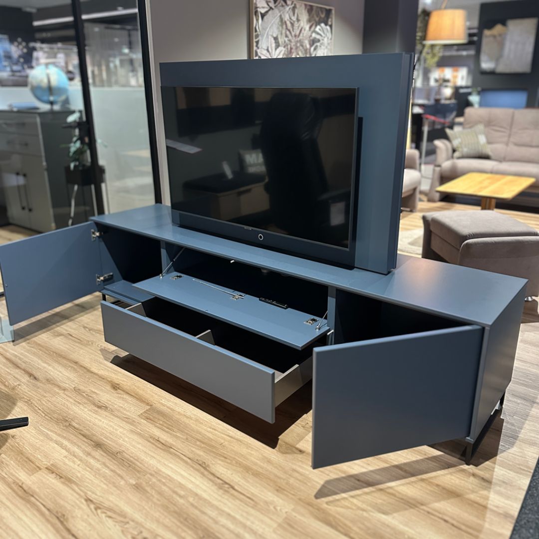 Moderner blauer TV-Schrank mit offenen Schranktüren und Schublade im Ausstellungsraum, der einen Fernseher integriert hat und zusätzlichen Stauraum bietet