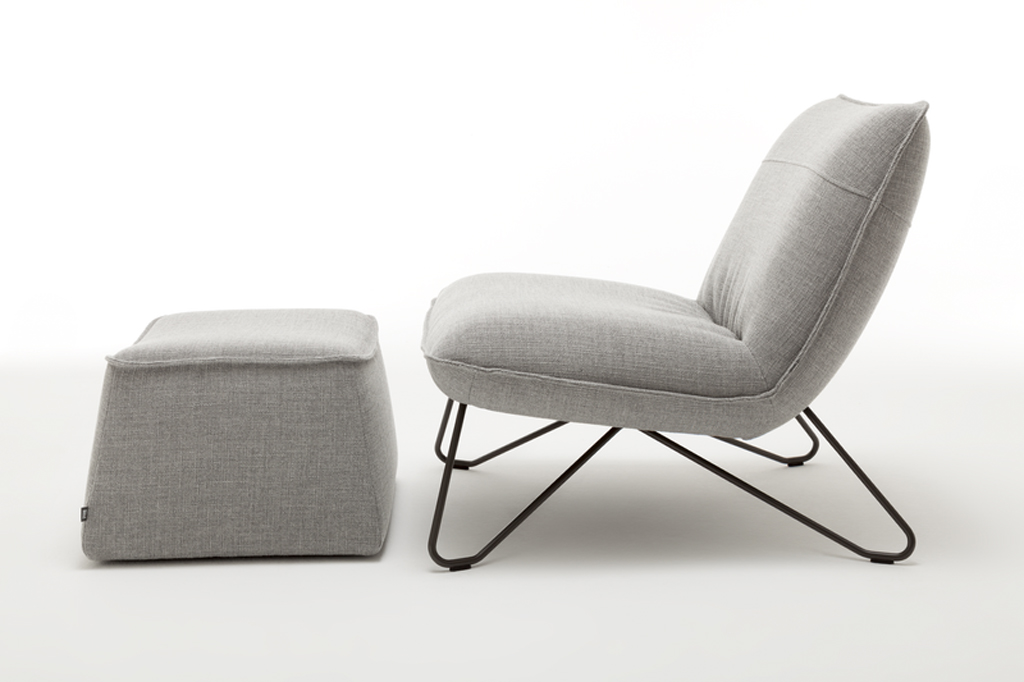 grauer designersessel mit schwarzen metallgestell und polsterhocker vor weißem Hintergrund