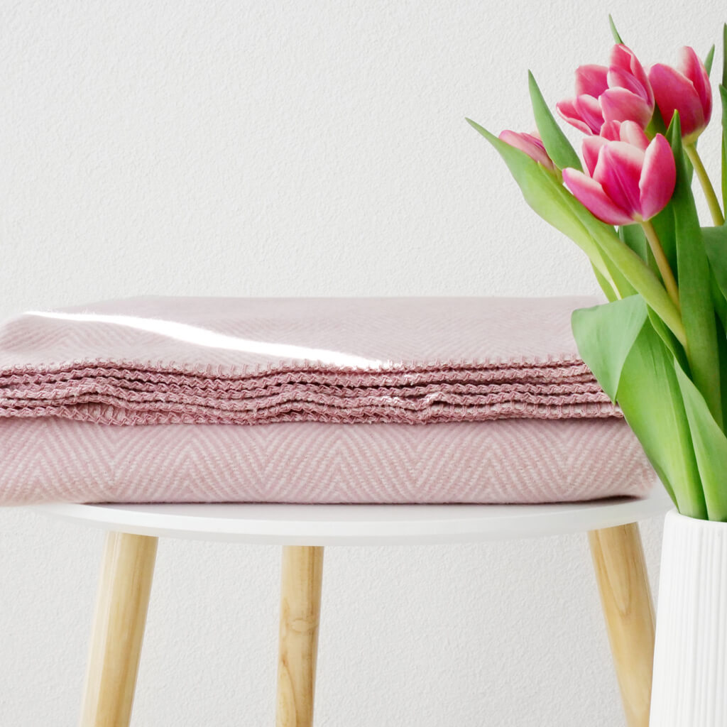 RIEMA. FINN – Wohndecke, Bio-Baumwolle - Fischgrät | 140 x 200 cm | rosa Gefaltete rosa Decke und Vase mit rosa Tulpen auf einem weißen Tisch