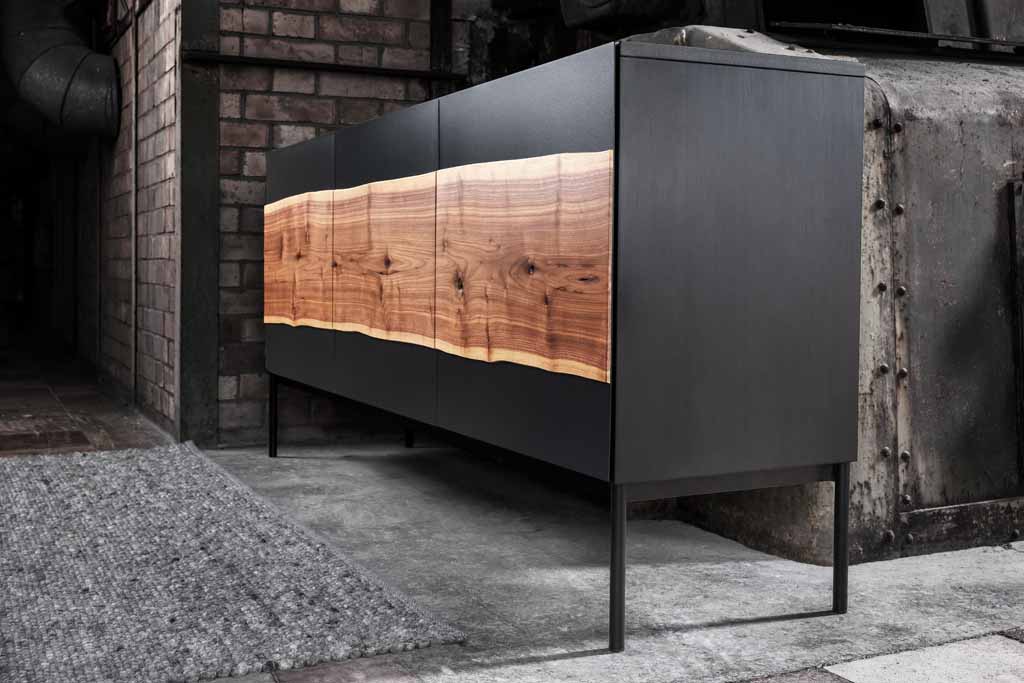 Ein modernes Sideboard mit dunklem Korpus und einer Front aus natürlichem Holz vor einer industriellen Wand