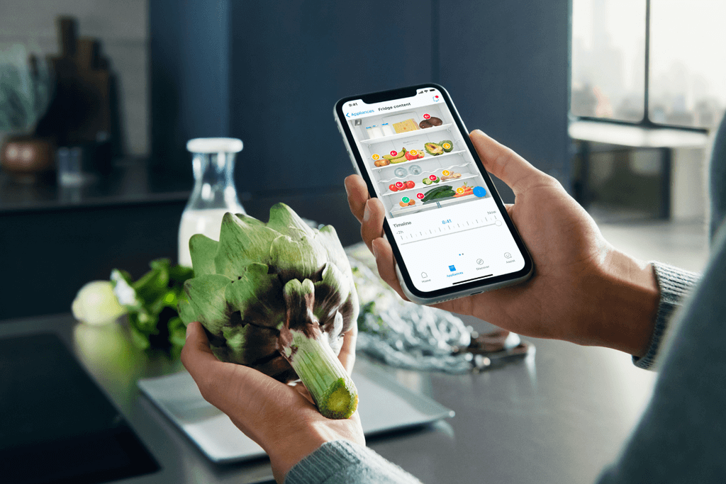 Person prüft den Inhalt seines Kühlschrankes mithilfe der HomeConnect App auf seinem Smartphone. 