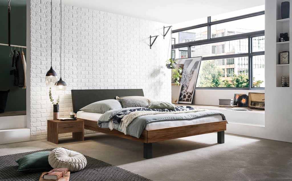 Helles Schlafzimmer mit modernem Holzbett, Nachttisch und dekorativen Kissen, großer Fensterfront und weißer Backsteinwand