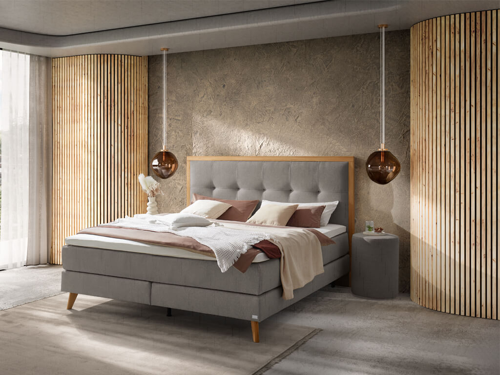 Ein Schlafzimmer, das ein hellgraues Boxspringbett mit einem karierten Kopfteil und dekorativen Kissen in einer warmen Atmosphäre zeigt.