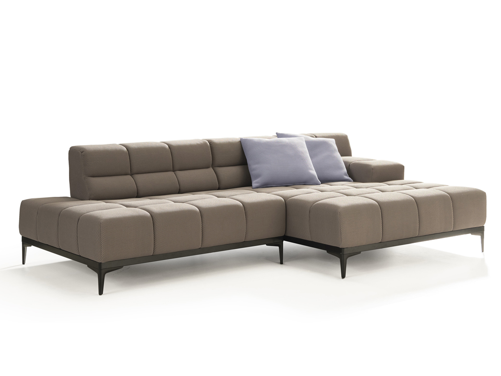Ein L-förmiges, modulares Ecksofa in Hellbraun mit einem feinen Punktmuster und gesteppten Sitz- und Rückenkissen. Es steht auf schlanken schwarzen Metallfüßen. Zwei hellblaue Zierkissen liegen auf der Rückenlehne. Der Hintergrund ist weiß.