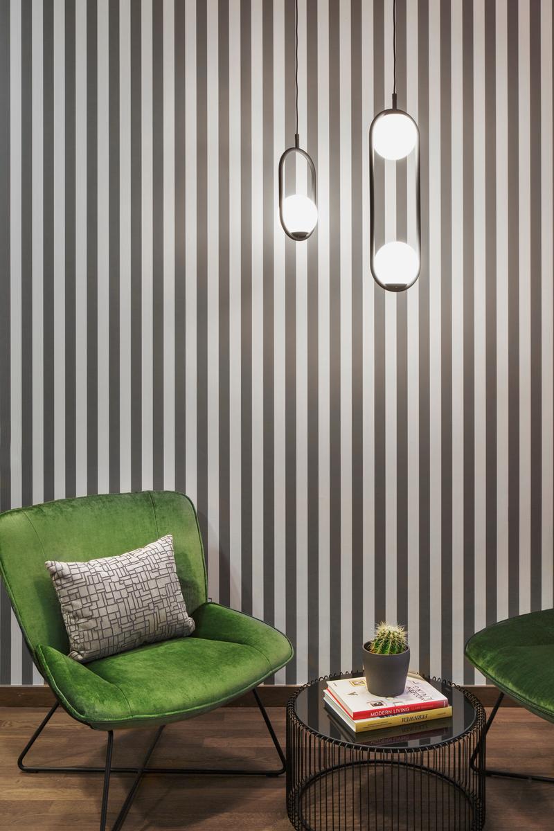 Ein stilvoll eingerichteter Raum mit grünen Stühlen, gestreifter Tapete, modernen Hängelampen und einem Tisch mit Büchern und einem Kaktus.