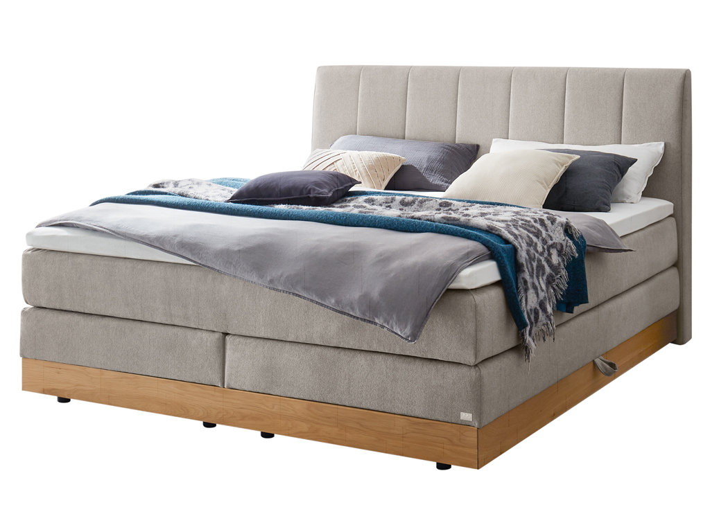 Ein Boxspringbett in hellem Grau mit einem gesteppten Kopfteil und einem Holzbettrahmen, freigestellt auf weißem Hintergrund.