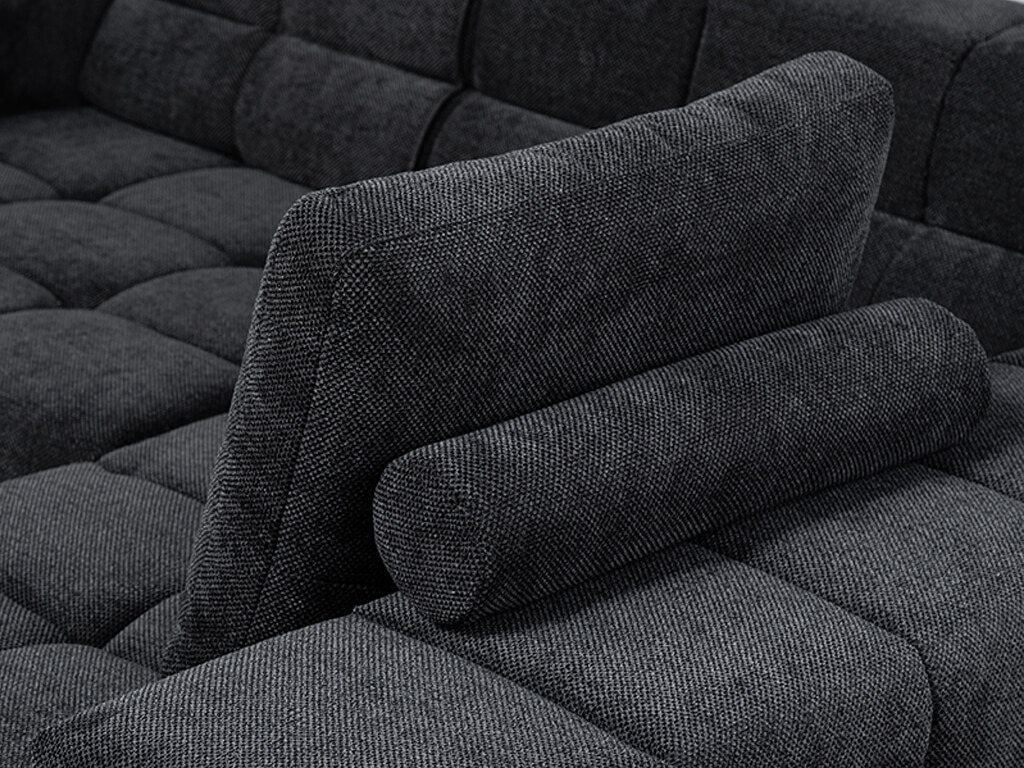 Nahaufnahme eines dunkelgrauen Sofas mit einem strukturierten Stoff. Ein aufrechtes Rückenkissen mit einer zylindrischen Nackenrolle davor ist zu sehen. Der Bezug des Sofas hat ein gestepptes, quadratisches Muster.