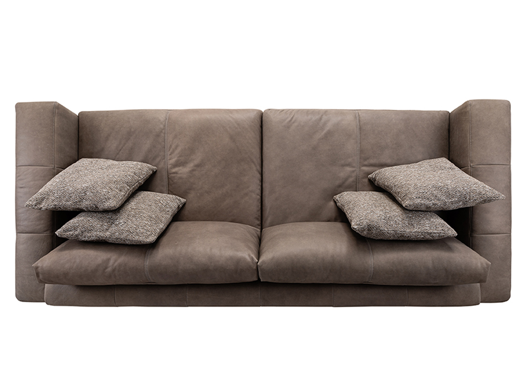 Eine Draufsicht auf ein braunes Ledersofa mit vier beigen, strukturierten Zierkissen auf den Sitzflächen.