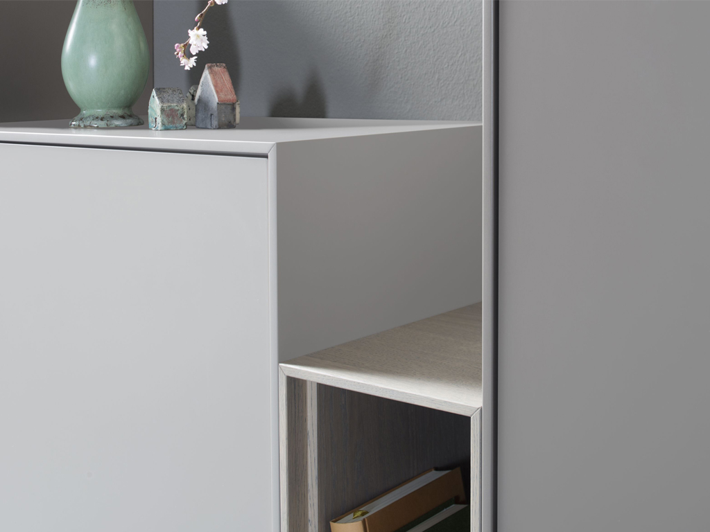 Detailansicht eines modernen grauen Schranks mit einer grünen Vase und kleinen Häuser-Dekorationen auf einer glatten Oberfläche