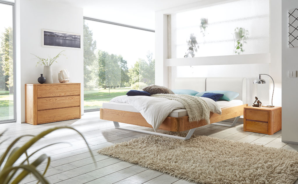 Modernes Bett mit braunem Rahmen und weißen Kufen und einem weißen Polsterkopfteil mit brauner Kommode und Nachtschrank mit Schubladen stilvoll dekoriert in einem modernen Zimmer