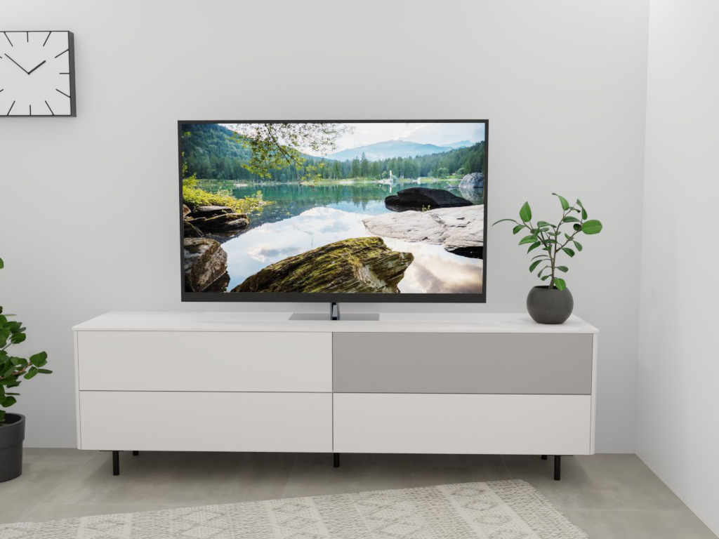 Sudbrock Goya - Lowboard mit Lochblechklappe | 2 Schubladen, 2 Klappen | B: 205,2 cm | Lack verkehrsweiß Ein Flachbildfernseher steht auf einem weißen Sideboard, daneben eine grüne Pflanze, im Hintergrund eine weiße Wand mit Uhr.
