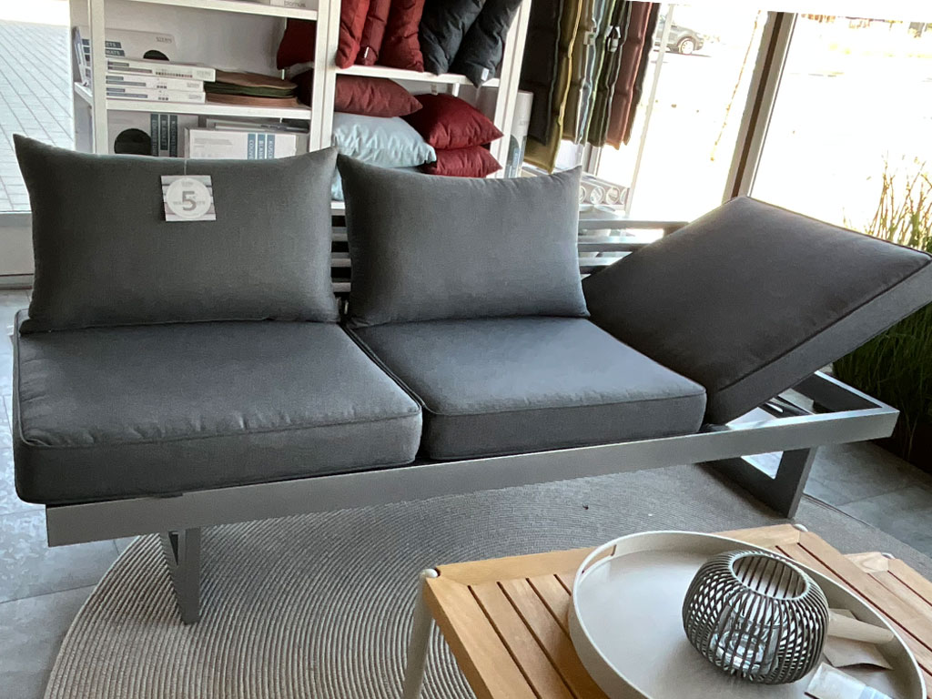 Dunkelgraues Polstersofa mit drei Sitzflächen, zwei Rückenkissen und hochgeklappter rechter Sitzfläche.