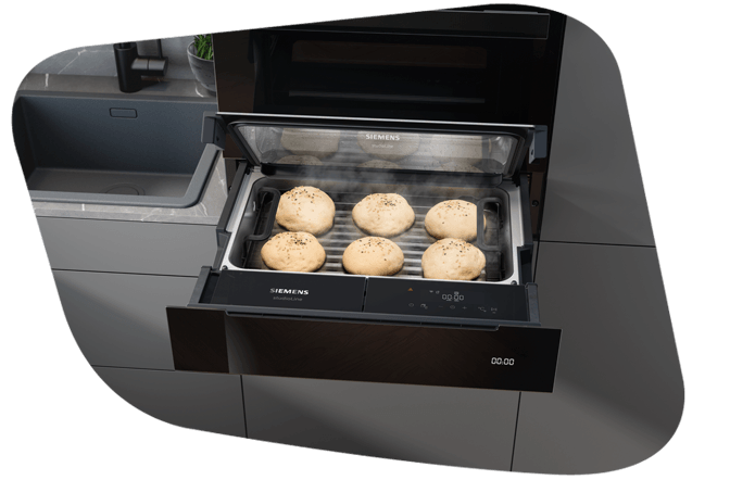 Sechs Hefeteig-Brötchen liegen auf einem Gitter in der Dampfschublade und gehen bei optimaler Feuchtigkeit und Temperatur gleichmäßig auf.