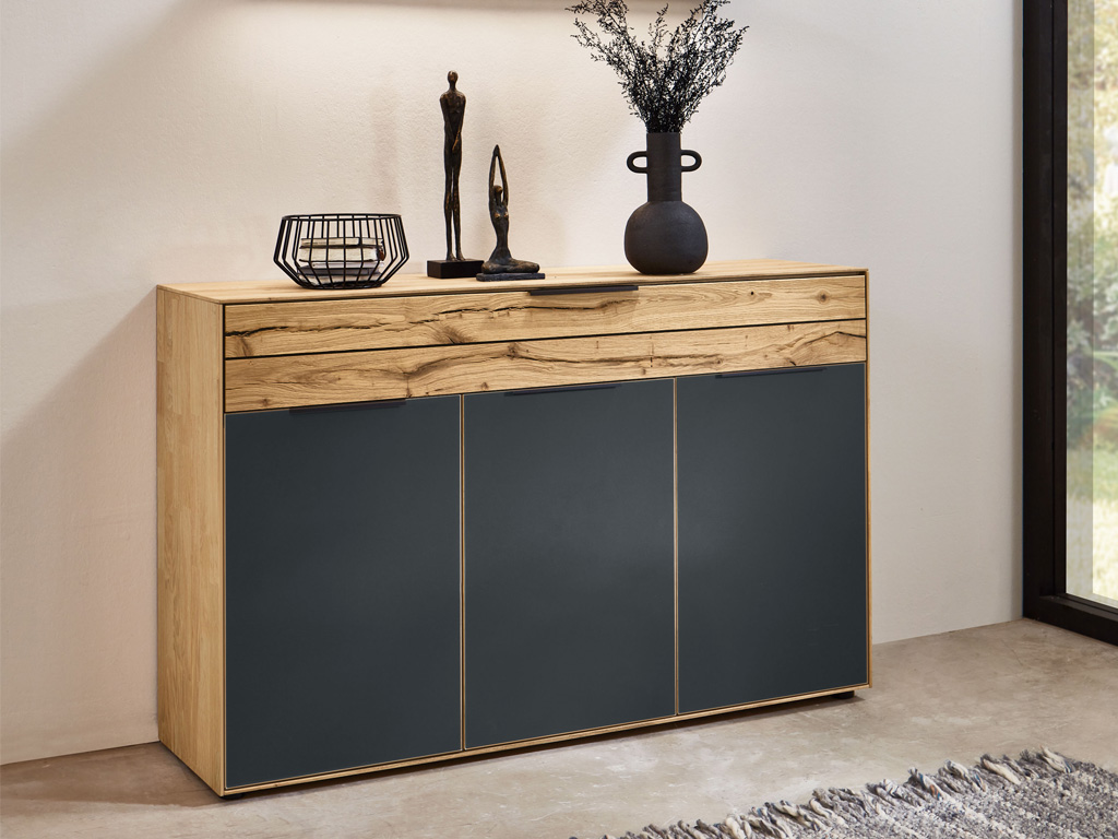 Wöstmann WSM 4300 - Kommode (2550) 1 Schubkasten, 3 Türen | Wildeiche massiv | B: 151,9 cm | konfigurierbar Elegante Kommode aus Holz mit dunklen Türen, dekoriert mit Statue und Vase in einem modernen Wohnambiente.