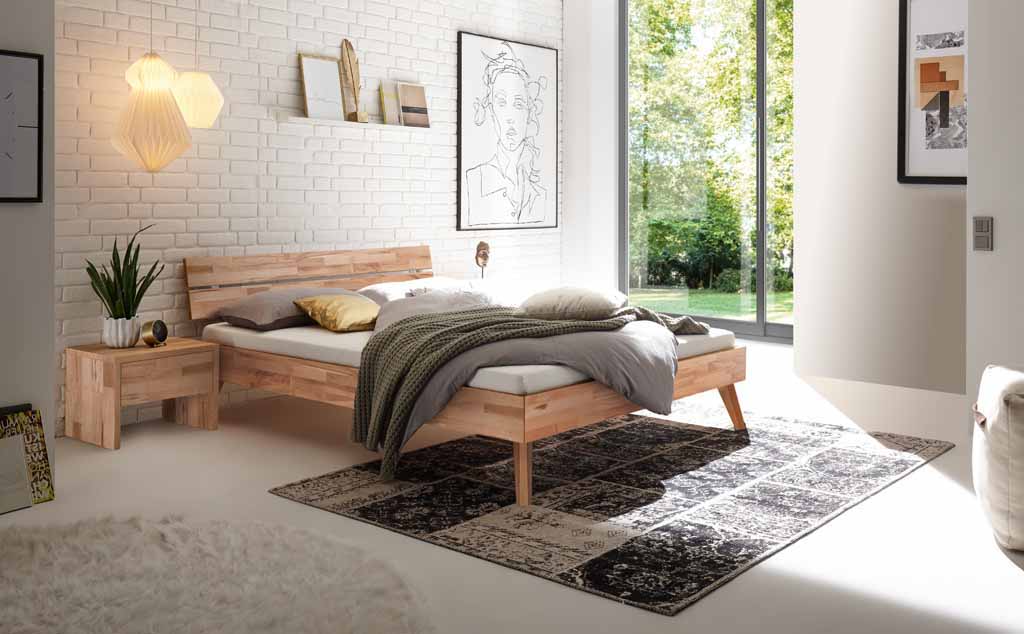 Hasena Trento - Bett Ortona | Kernbuche natur, geölt Schlafzimmer mit Holzbett, Nachttisch, dekorativen Kissen, großem Fenster und stilvollem Teppich