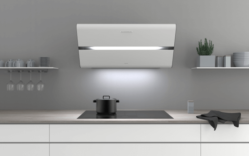 Eine moderne, weiße Kopffreihaube von Berbel ist prominent über einem schwarzen Induktionskochfeld platziert. Sie verfügt über eine integrierte horizontale LED-Beleuchtung, die den Kochbereich optimal ausleuchtet.