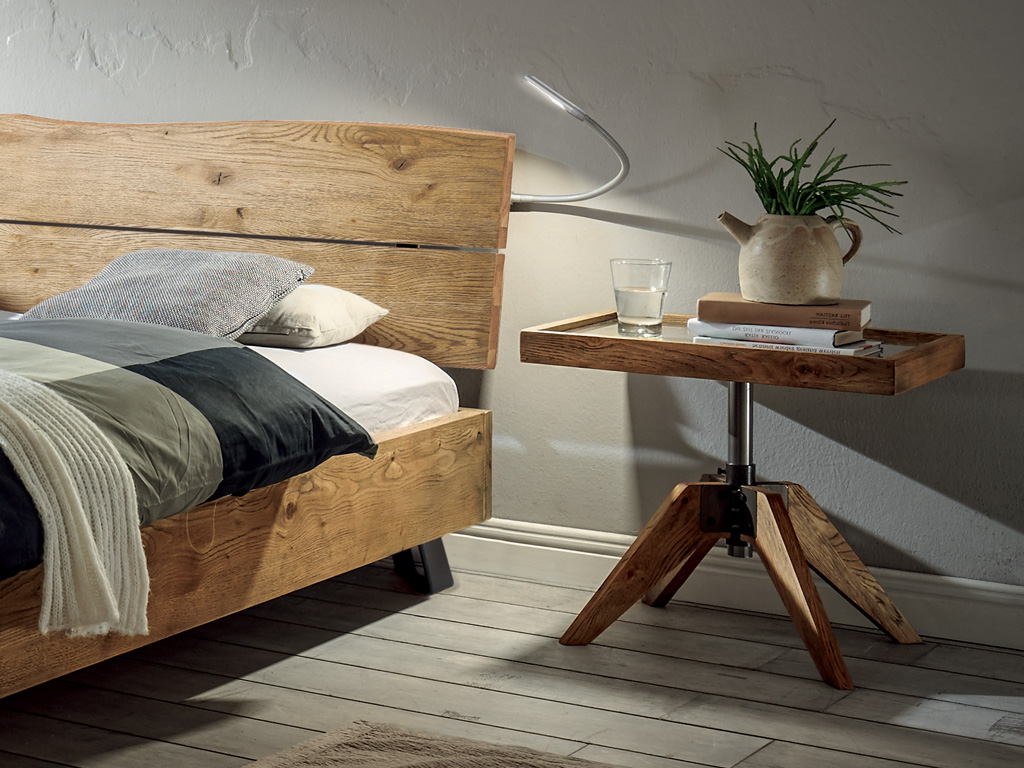 brauner exklusiver Holznachttisch auf dreibeinfüßen und einer Platte in Tablettform mit Glasablage stilvoll dekoriert an einem Bett Hasena Carpi 