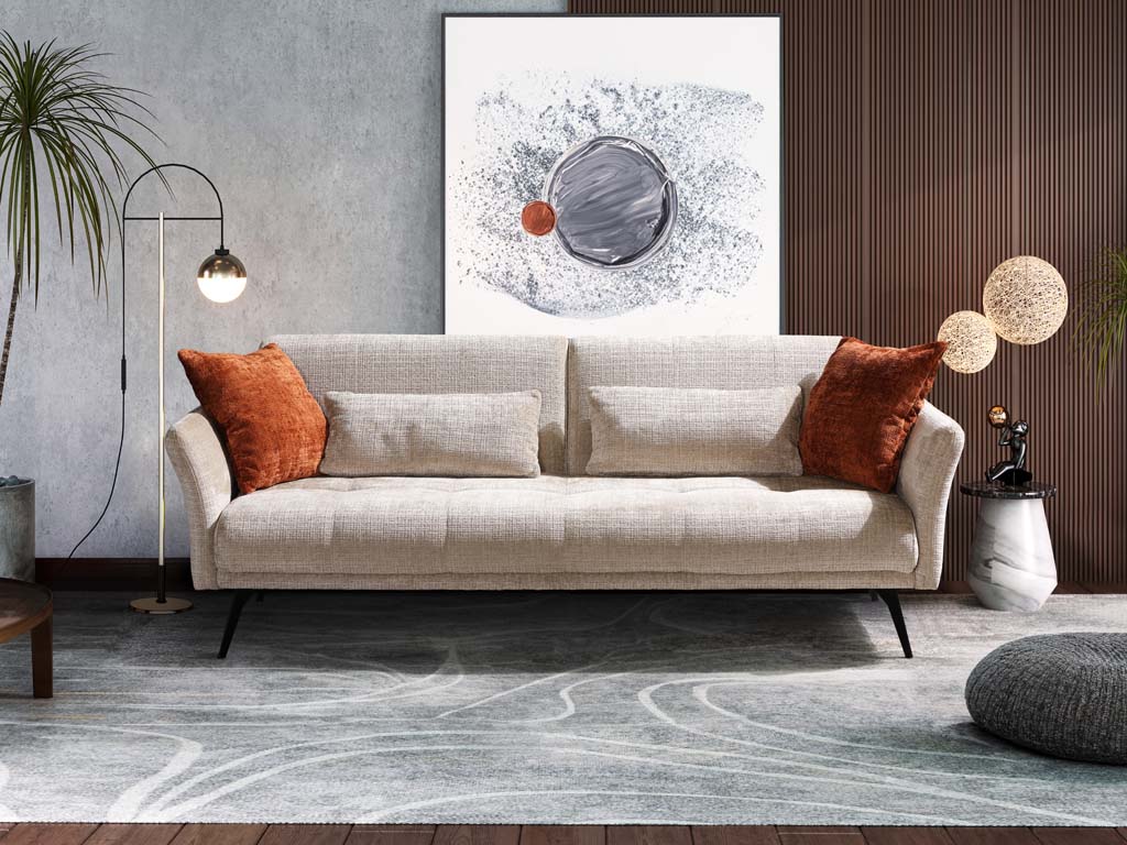 Restyl Amber -Schlafsofa (Querschläfer) | beige | mit Armteilen | inkl. Kissen | 130 x 200 cm Ein modernes Wohnzimmer mit einem hellen Sofa, dekoriert mit orangefarbenen Kissen. Im Hintergrund ein abstraktes Kunstwerk, flankiert von Pflanzen und einer Stehlampe.