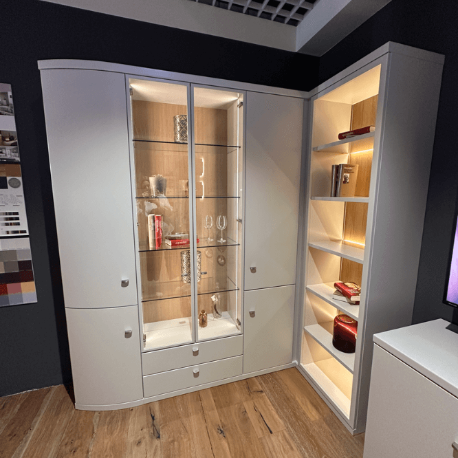 Weißer Eckvitrinenschrank mit Glastüren, beleuchtetem Inneren und seitlichen Regalböden in einem modernen Wohnraum
