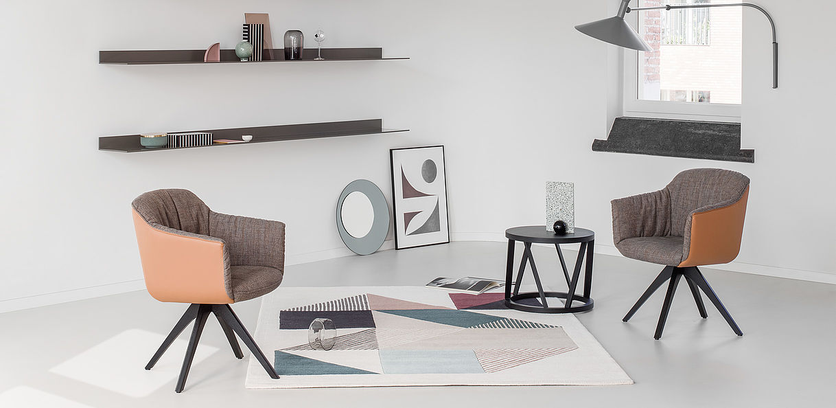 Ein stilvoll eingerichtetes Wohnzimmer mit zwei modernen Sesseln, einem runden Couchtisch und dekorativen Regalen an der Wand.